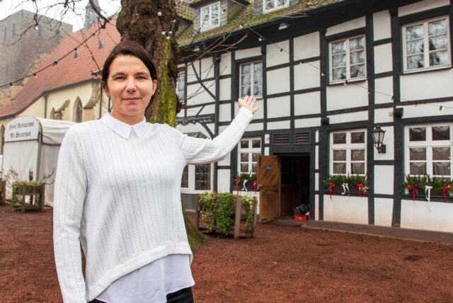 Tatjana Schüle steht vor dem Alt Westerholt in Herten und deutet mit einer Hand auf das Restaurant.