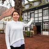 Tatjana Schüle steht vor dem Alt Westerholt in Herten und deutet mit einer Hand auf das Restaurant.