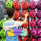 Ein Verkäufer sortiert bei Decathlon Fahrradhelme, hinein montiert ist der Schriftzug „Usermeinung“