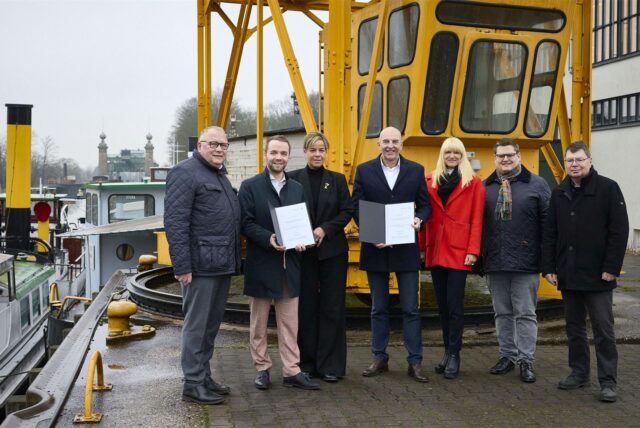 Waltrops Bürgermeister Marcel Mittelbach und LWL-Direktor Dr. Georg Lunemann halten am Schiffshebewerk Henrichenburg in Waltrop die Förderbescheide, die ihnen NRW-Wirtschaftsministerin Mona Neubaur übergeben hatte.