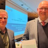 Stefan Kuczera und Markus Gerber vom RVR lächeln vor dem Hintergrund von Planungsunterlagen in die Kamera.