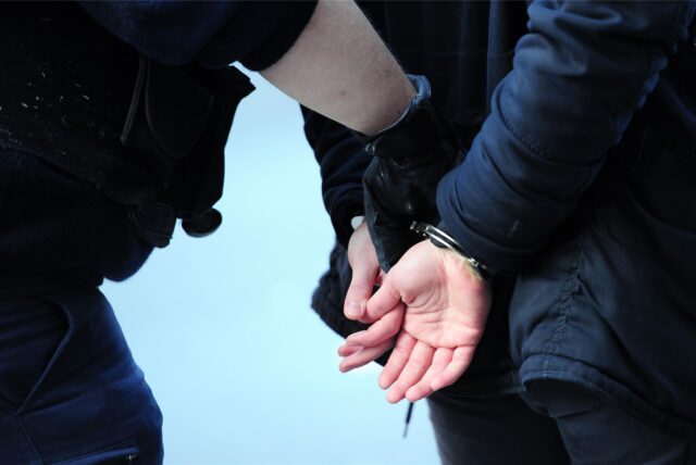 Um die Hände eines Mannes sind Handschellen, eine Polizist greift nach diesen. (Symbolbild)