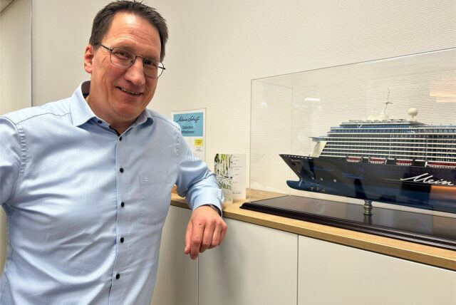 Michael Germann steht in seinem Reisebüro in Herten-Disteln neben dem Modell eines Kreuzfahrtschiffes.