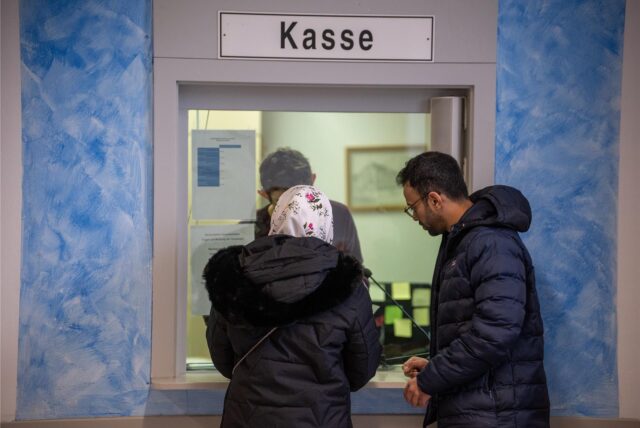 Zwei Personen – offenbar mit Migrationshintergrund – stehen an einer Kasse