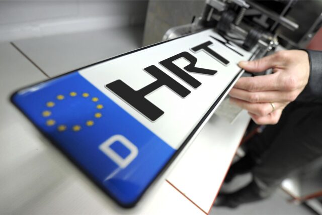 Eine Hand zieht ein Kfz-Kennzeichen mit der Aufschrift HRT aus einer Druckmaschine.