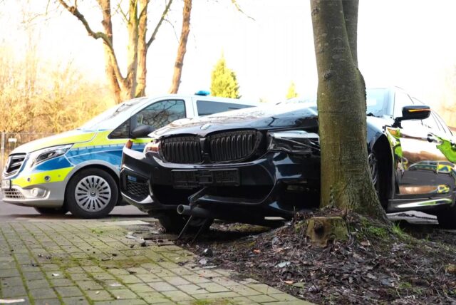 Unfall in Herten: Ein schwarzer BMW ist vor einen Baum geprallt. Dahinter steht ein Polizeiauto.