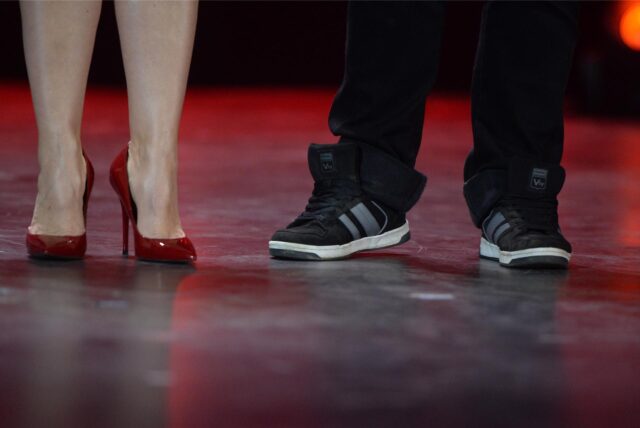 Auf einem roten Teppich stehen ein Mann, der Turnschuhe anhat. Links neben ihm eine Frau mit roten  Pumps.