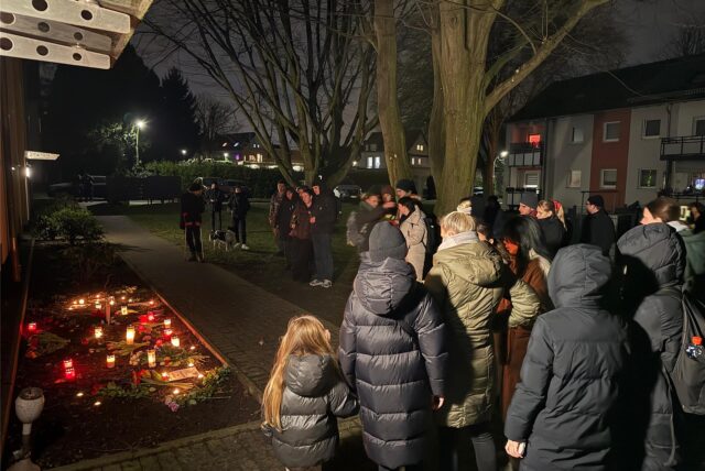 Mehrere Menschen versammeln sich vor der Wohnung, in der eine 32-jährige Dortmunderin mutmaßlich von ihrem Ex-Partner ermordet worden ist. Kerzen sind vor dem Haus aufgestellt.