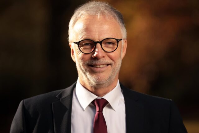 Hertens Bürgermeister Matthias Müller, im dunklen Anzug mit weinroter Krawatte und weißem Hemd, lächelt in die Kamera.