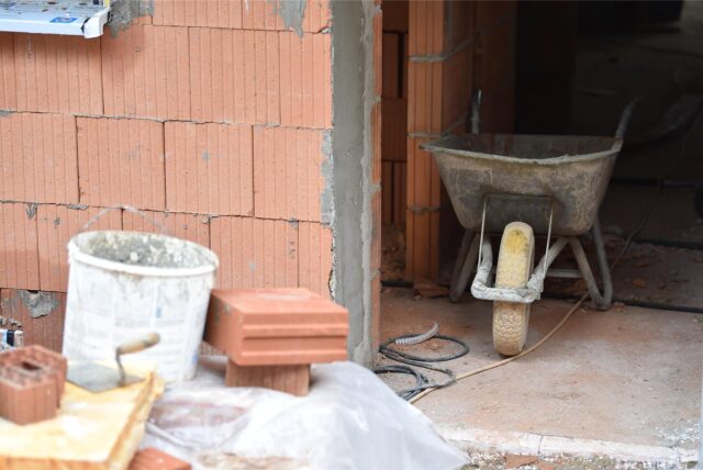Eine Schubkarre, Steine, Maurerkelle und ein Mörteleimer stehen auf einer Baustelle. (Symbolbild)