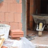 Eine Schubkarre, Steine, Maurerkelle und ein Mörteleimer stehen auf einer Baustelle. (Symbolbild)