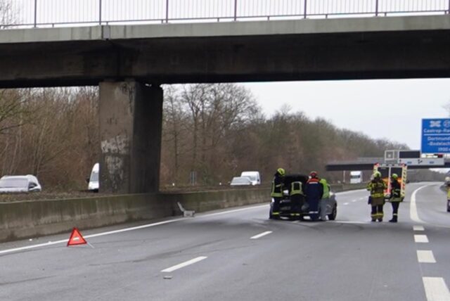 Bremsspuren auf der linken Fahrbahn, ein Warndreieck und das stehengebliebene Auto mit Einsatzkräften der Feuerwehr auf der A 42.