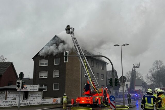 Feuerwehrleute stehen an einem Mehrfamilienhaus.