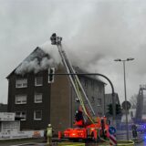 Feuerwehrleute stehen an einem Mehrfamilienhaus.