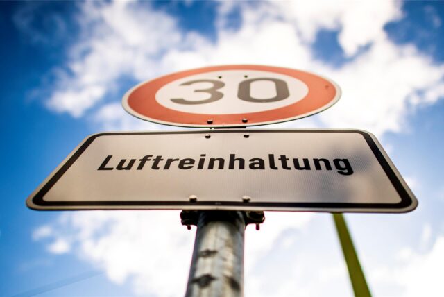 Vor blauem Himmel steht ein Tempo-30-Schild mit einem Luftreinhaltungshinweis