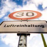 Vor blauem Himmel steht ein Tempo-30-Schild mit einem Luftreinhaltungshinweis