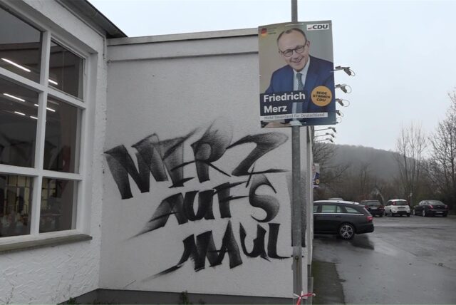 Auf der Schützenhalle Hüingsen steht die aufgesprühte Parole „Merz aufs Maul“ neben einem Plakat mit dem Spitzenkandidaten der CDU Friedrich Merz.