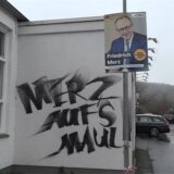 Auf der Schützenhalle Hüingsen steht die aufgesprühte Parole „Merz aufs Maul“ neben einem Plakat mit dem Spitzenkandidaten der CDU Friedrich Merz.