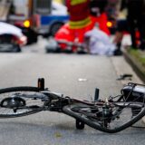 Verunfalltes Fahrrad auf der Straße, im Hintergrund Rettungskräfte.