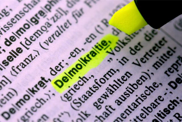 In einem Lexikon wird der Begriff „Demokratie“ gelb unterstrichen.