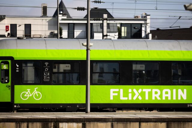 Ein grüner Flixtrain-Wagon mit schwarzem Fensterband und grauem Dach. Links ist die Einstiegstür zu erkennen, danaben ist ein Piktogramm eines Fahrrades aufgedruckt.