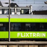 Ein grüner Flixtrain-Wagon mit schwarzem Fensterband und grauem Dach. Links ist die Einstiegstür zu erkennen, danaben ist ein Piktogramm eines Fahrrades aufgedruckt.