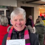 Esther Eckes steht unter dem Arkadendach in Marl Hüls auf der Hülsstraße. Sie lächelt in die Kamera. Im Hintergrund steht eine Gruppe Menschen unter dem Vordach.