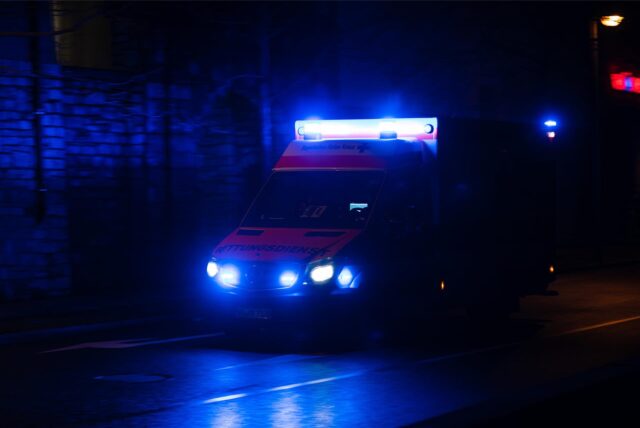 Ein Krankenwagen fährt nachts mit Blaulicht durch eine Straße.
