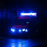 Ein Krankenwagen fährt nachts mit Blaulicht durch eine Straße.