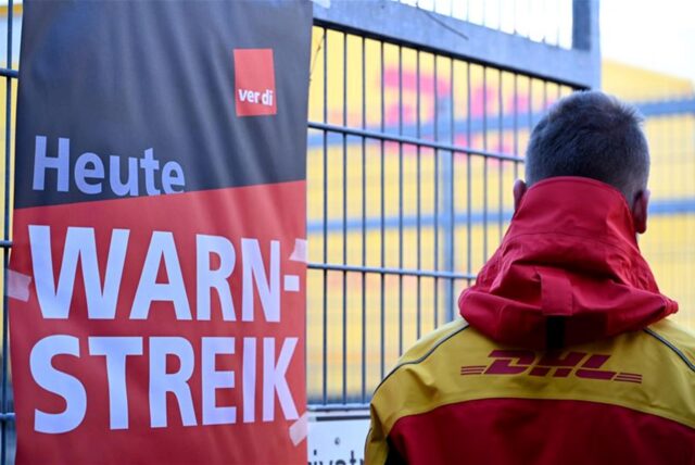 Streikposter am Werkstor: Ein DHL-Mitarbeiter hat die Arbeit niedergelegt und schaut auf eine Zustellbasis, in der er sonst arbeitet.