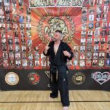 Chris Stallmann steht vor einer Wand mit der Aufschrift „MAA“. Das steht für Martial Arts