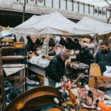 Menschen durchstöbern verschiedene Stände mit Gebrauchtgegenständen auf einem Trödelmarkt.
