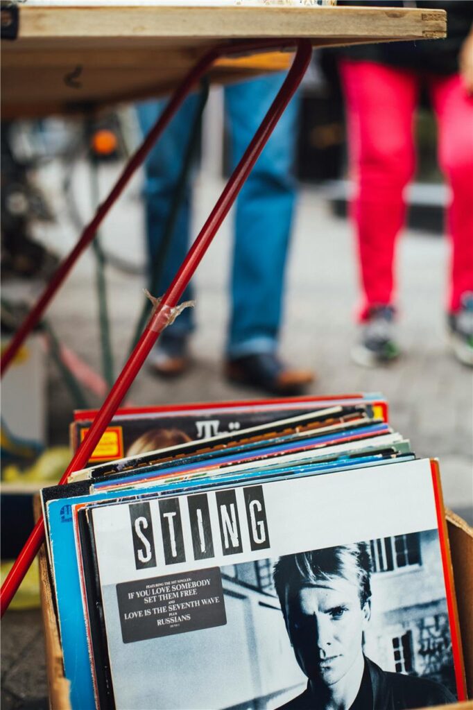 Neben einem Stand auf einem Trödelmarkt steht eine Kiste mit Schallplatten.