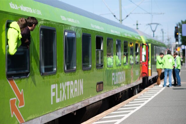 Ein grüner Zug von Flixtrain steht an einem Bahngleis.