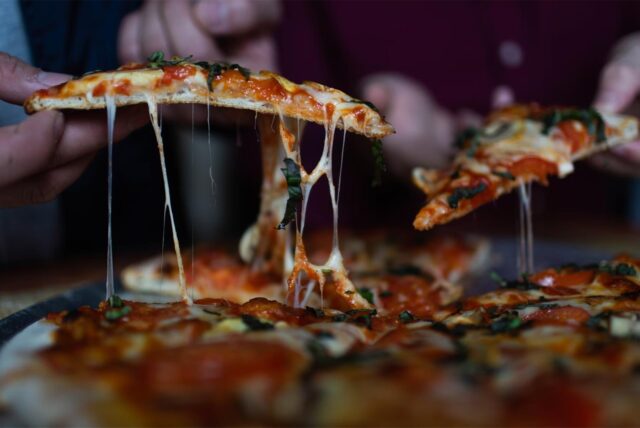 Zwei Personen ziehen zwei Stücke aus einer Pizza.
