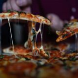 Zwei Personen ziehen zwei Stücke aus einer Pizza.