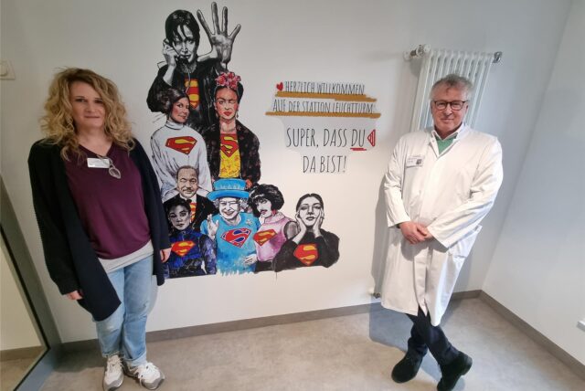 Prof. Boris Zernikow und Stationsleiterin Alexandra Tüllmann stehen auf der Schmerzstation der Kinderklinik vor einem der vielen neuen Superheld:innen-Wandmotive.