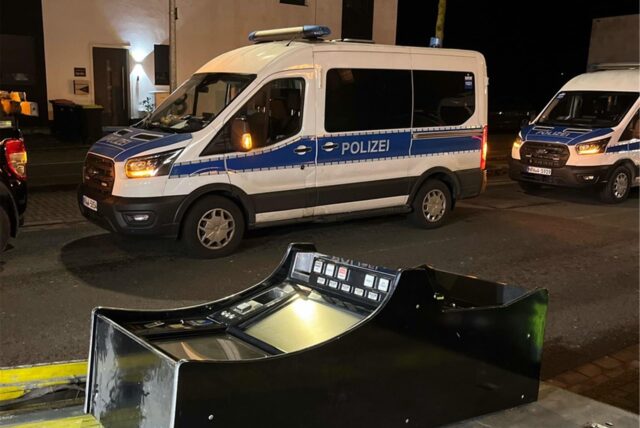 Ein Spielautomat liegt vor einem Polizei-Einsatzfahrzeug.