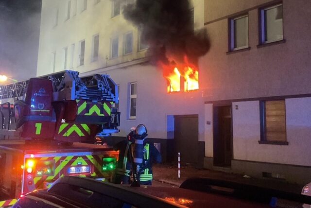 Einsatzkräfte der Feuerwehr Dortmund löschen ein Feuer, dichter Rauch kommt aus der Brandwohnung.