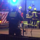Polizisten mit dem Rücken zur Kamera, im Hintergrund Feuerwehrkräfte an einem Löschfahrzeug.