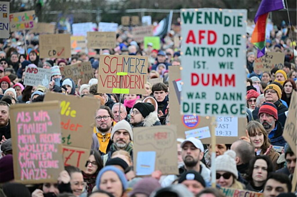 Menschen halten während einer Demonstration in Berlin unter dem Motto „Aufstand der Anständigen - Demo für die Brandmauer“ Schilder hoch, auf denen unter anderem „Schmerz verhindern“ steht.