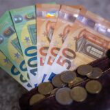 Geldscheine mit dem Wert von 100 und 50 Euro stecken in einem Geldbeutel, während auf dem Geldbeutel Münzen liegen.