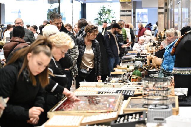 Mehrere Menschen studieren die Auslage bei einem Trödelstand im Marler Stern. Auf dem Tisch liegen Kassetten mit Schmuck. Man erkennt Ringe und Ketten. Im Hintergrund ist der Ausgang Richtung Rathaus zu sehen.