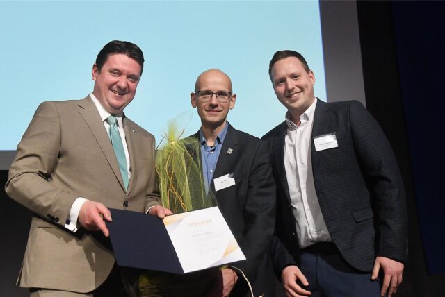 Bürgermeister Rajko Kravanja (links) und Redaktionsleiter Fabian Hollenhorst (rechts) würdigen Marc Frese mit der Verleihung der Ehrennadel.
