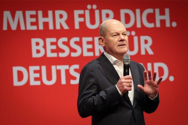 Bundeskanzler Olaf Scholz mit einem Mikrofon in der Hand vor einem SPD-Wahlkampf-Plakat bei einer Wahlkampfveranstaltung.