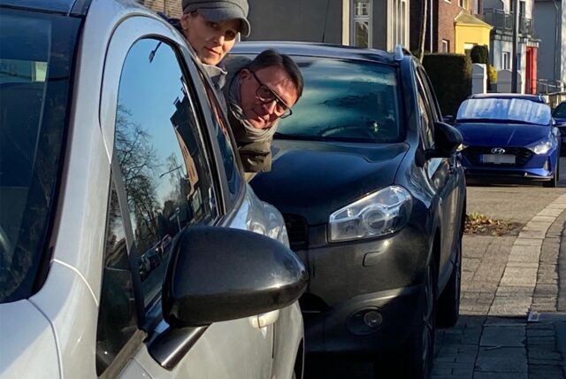 Nadine Weber-Mau und Michael Schiller schauen auf der engen Gartenstraße in Herten-Mitte zwischen parkenden Autos hindurch, ob die Fahrbahn frei ist.