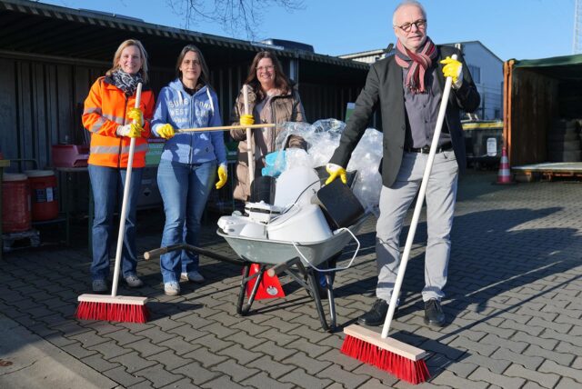 Mitarbeiterinnen des ZBH, eine stellvertretende Bürgermeisterin und der Bürgermeister stehen mit Besen in der Hand an einer Schubkarre voller Müll.