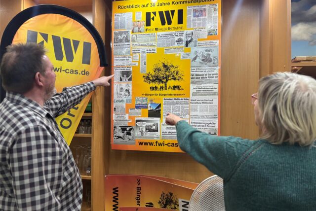 Wolfgang Limberg und Hildegard Krusch betrachten das Plakat, das die FWI zum 30-Jährigen bastelte: eine Collage der Zeitungsberichte, die Erfolge dokumentieren.
