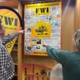 Wolfgang Limberg und Hildegard Krusch betrachten das Plakat, das die FWI zum 30-Jährigen bastelte: eine Collage der Zeitungsberichte, die Erfolge dokumentieren.
