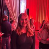 Friederike Kraft steht in der LaVictoria Halle in Marl. Die Beleuchtung ist sehr rot. Sie lächelt in die Kamera. Im Hintergund sind weitere Schülerinnen und Schüler des Gymnasiums im Loekamp zu erkennen.